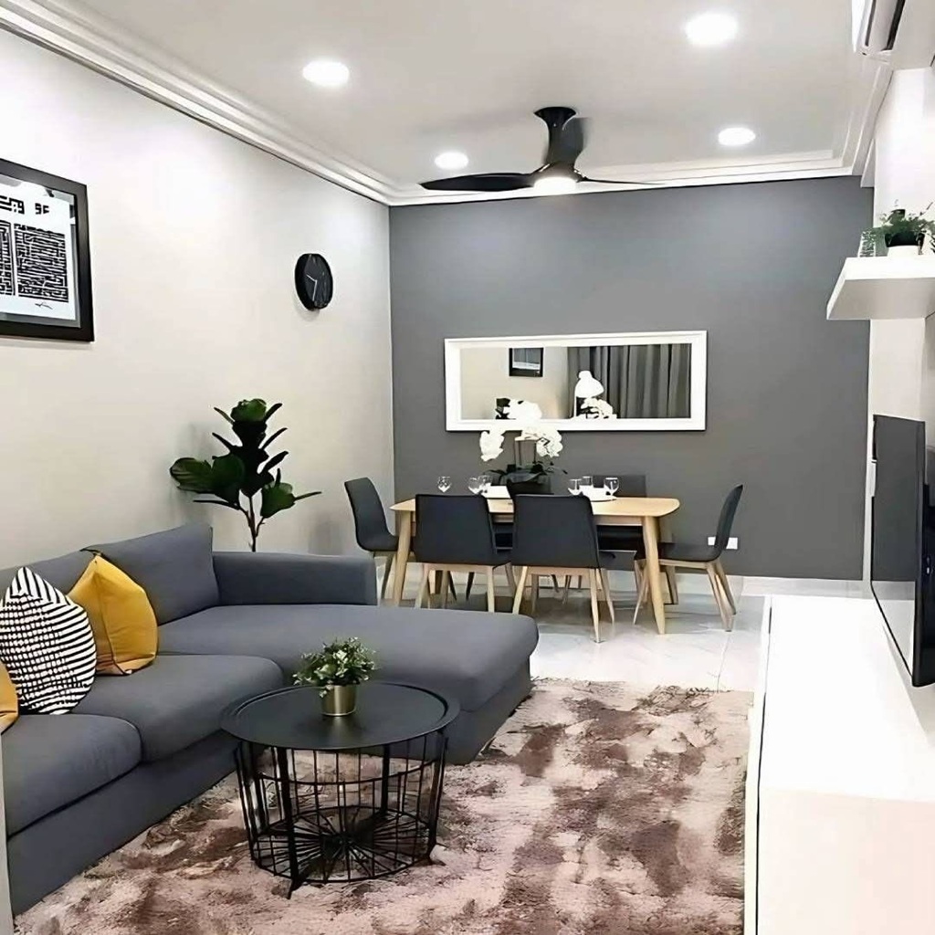 Salón comedor moderno y minimalista con sofá gris, cojines amarillos, mesa auxiliar negra, pared gris con espejo decorativo y comedor de madera con sillas oscuras en un espacio pequeño y bien iluminado.